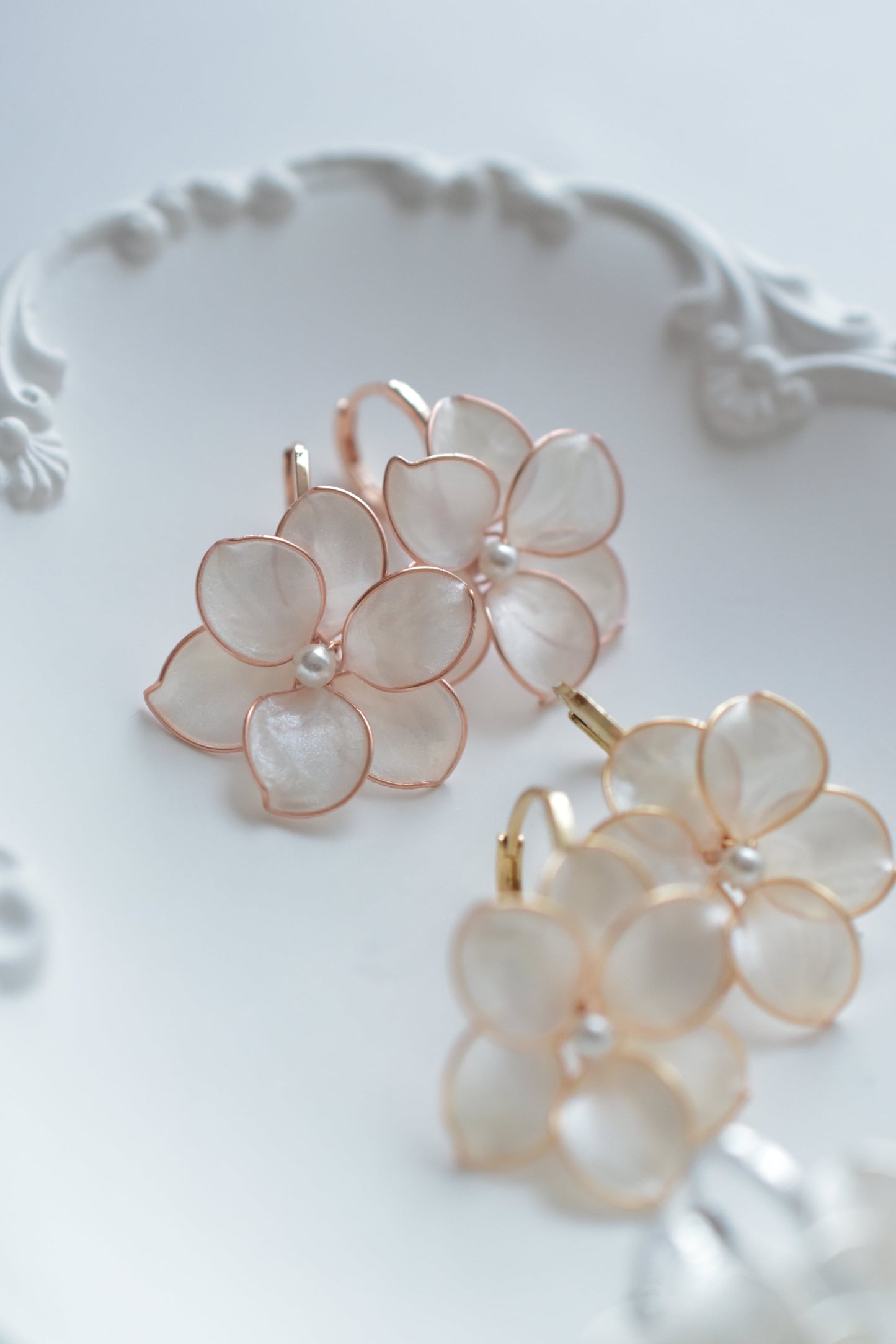 Pair of floral earrings in rose gold and gold dainty and elegant on a decorative white plate, suitable bridesmaid and bridal earrings wedding jewelry